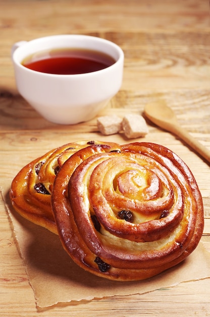 Panini freschi con uvetta e tazza di tè caldo su tavola in legno rustico