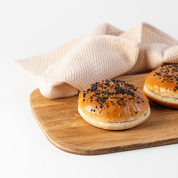 Panini per hamburger con semi di sesamo su una tavola di legno su sfondo bianco, primo piano