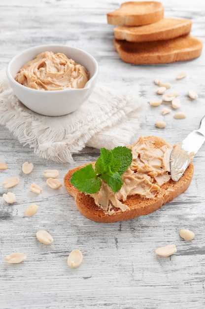 Panino Al Burro Di Arachidi. Decorato con menta. In fondo è una tazza con burro di arachidi e pane.