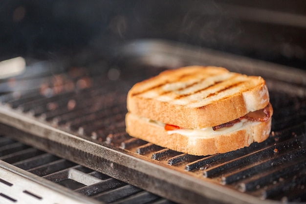 Panino al formaggio grigliato alla griglia con strisce di pancetta e pomodoro fresco sulla griglia a gas all'aperto.