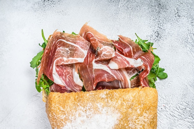 Panino al prosciutto di Parma su pane ciabatta con rucola. Tavolo bianco. Vista dall'alto.