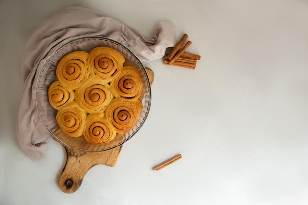 panino alla cannella con glassa e bastoncini di cannella con un bicchiere di latte su uno sfondo grigio chiaro vista dall'alto