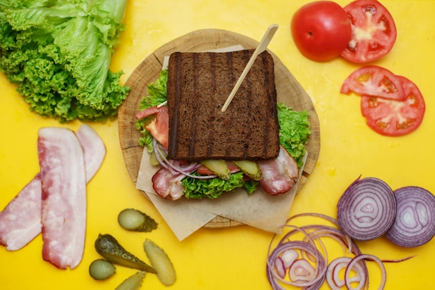 Panino arrostito del pane scuro sul piatto di legno sul bordo giallo