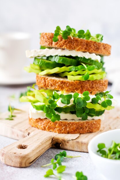 Panino con avocado, cetriolo e feta decorato con micro-verdure e pane multicereali su un semplice supporto in legno per una sana colazione. Messa a fuoco selettiva