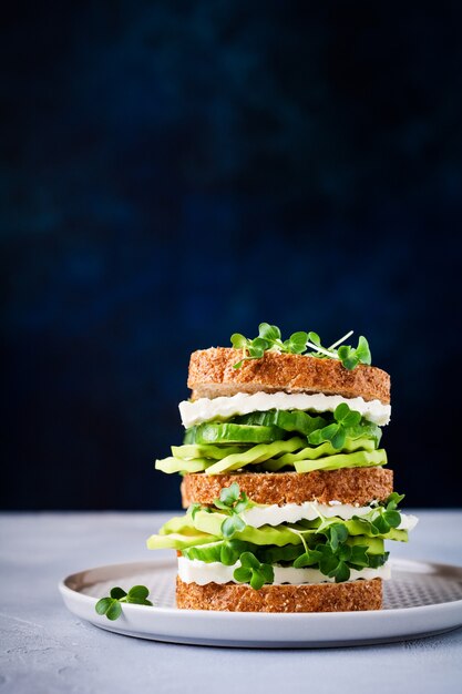 Panino con avocado, cetriolo e formaggio feta decorato con micro-verdure e pane ai cereali su un semplice supporto in legno per una colazione sana