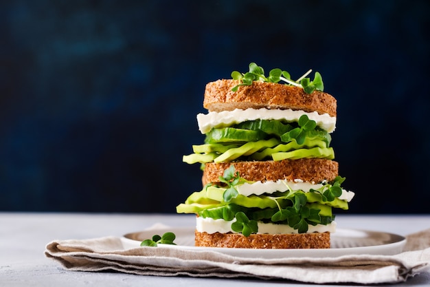 Panino con avocado, cetriolo e formaggio feta decorato con micro-verdure e pane ai cereali su un semplice supporto in legno per una colazione sana