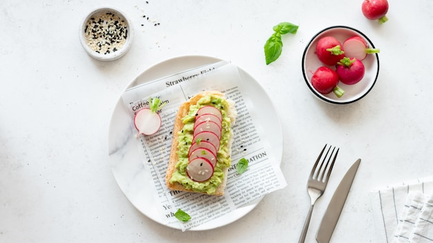 Panino con avocado, fette di ravanello, semi di sesamo e basilico in un piatto su carta pergamena. concetto di cibo vegetariano.