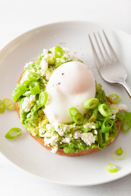 Panino con avocado per colazione con uovo in camicia e formaggio feta