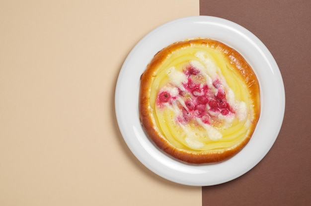 Panino con crema pasticcera e ribes rosso in piatto su uno sfondo colorato, vista dall'alto con spazio per le copie