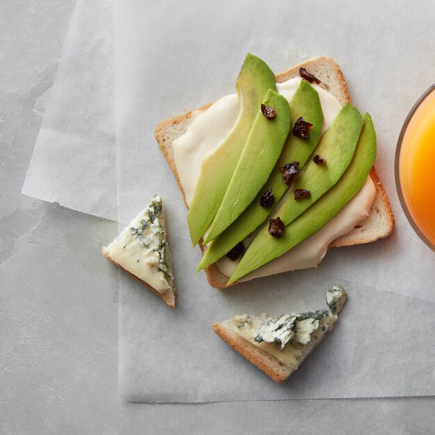 Panino con formaggio e avocado e arancia fresco su carta e tavolo in cemento grigio