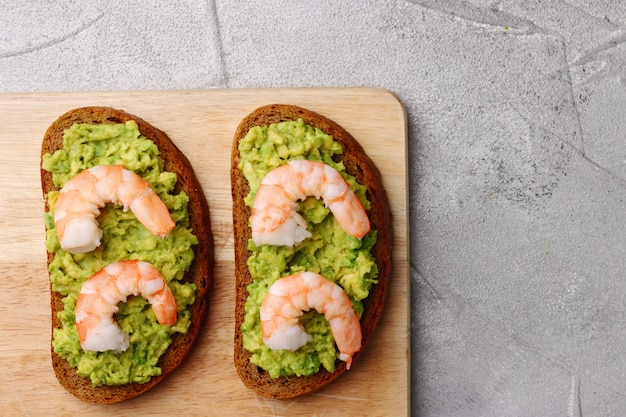 Panino con guacamole e gamberetti su sfondo di cemento