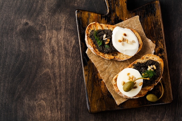 Panino con la fetta di mozzarella e tapenade sul fondo rustico scuro della tavola