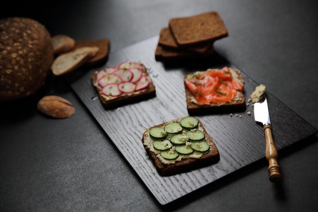 Panino con pane ai cereali, salmone affumicato, barbabietola e cetriolo su fondo di marmo scuro