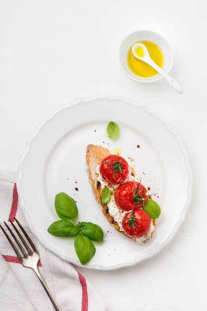 Panino con pomodorini al forno, aglio, olio d'oliva e ricotta su superficie bianca