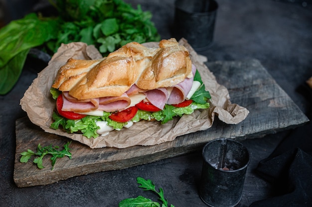 Panino con prosciutto formaggio pomodoro e lattuga su fondo scuro