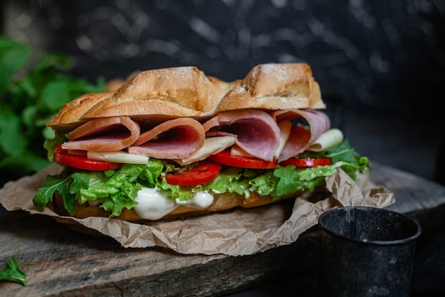 Panino con prosciutto formaggio pomodoro e lattuga su fondo scuro