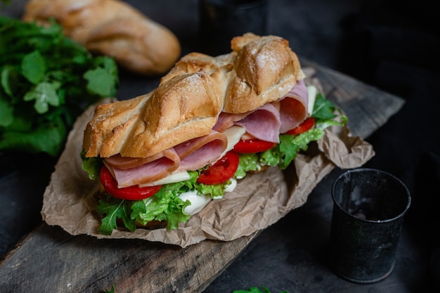 Panino con prosciutto formaggio pomodoro e lattuga su fondo scuro