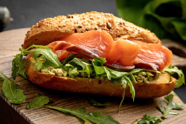 Panino con salmone e rucola servito su una tavola di legno su fondo scuro