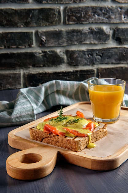 Panino con salmone, formaggio fuso e salsa piccante e un bicchiere di succo d'arancia