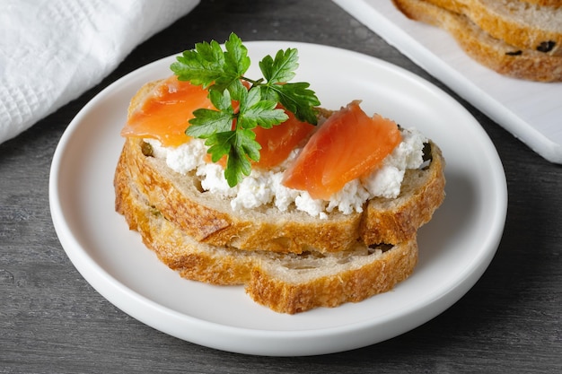 Panino con salmone salato e ricotta su un tavolo di legno grigio