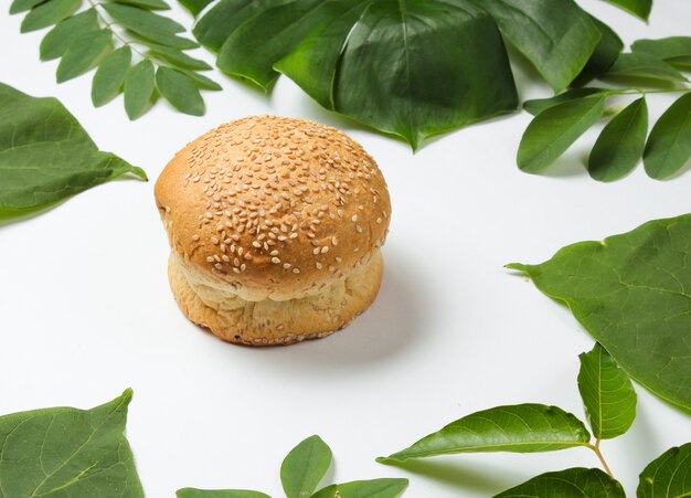 Panino con semi di sesamo su uno sfondo bianco con foglie verdi tropicali