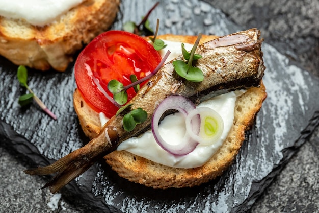 Panino con spratti pomodori cipolla e microgreen su una tavola di ardesia Cucina danese Sfondo ricetta alimentare Primo piano