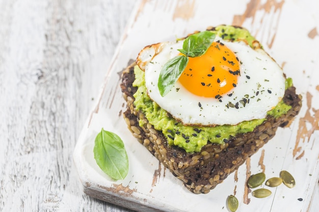 Panino con uovo di avocado e spinaci su fondo di legno bianco dieta sana colazione