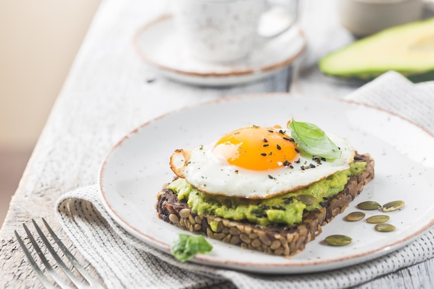 Panino con uovo di avocado e spinaci su fondo di legno bianco dieta sana colazione