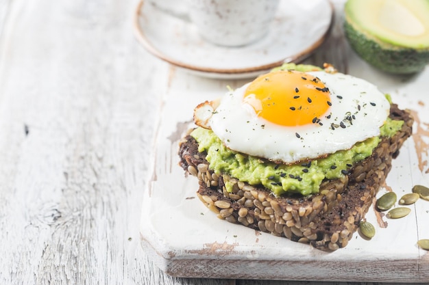 Panino con uovo di avocado e spinaci su fondo di legno bianco dieta sana colazione
