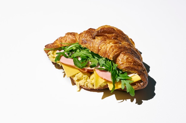 Panino croissant con mortadella, formaggio, rucola e uova strapazzate. Luce forte. sfondo bianco