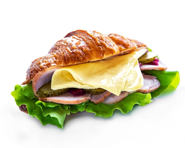 Panino croissant con prosciutto, formaggio e lattuga su una superficie bianca