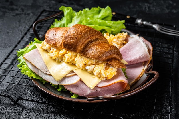 Panino croissant per la colazione con uova strapazzate formaggio e prosciutto Sfondo nero Vista dall'alto