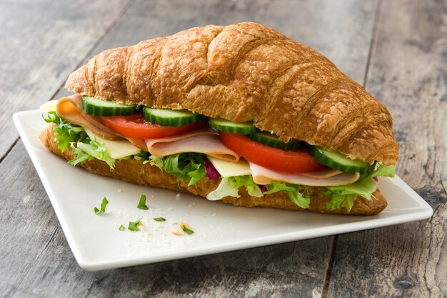 Panino del croissant con formaggio, il prosciutto e le verdure sulla tavola di legno