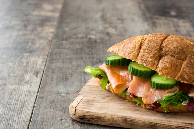 Panino del croissant con i salmoni e le verdure sullo spazio di legno della copia della tavola