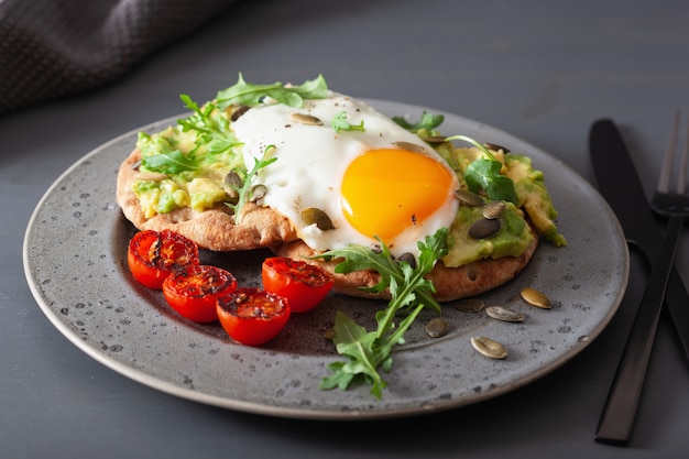 Panino dell'avocado della prima colazione con l'uovo fritto e il pomodoro