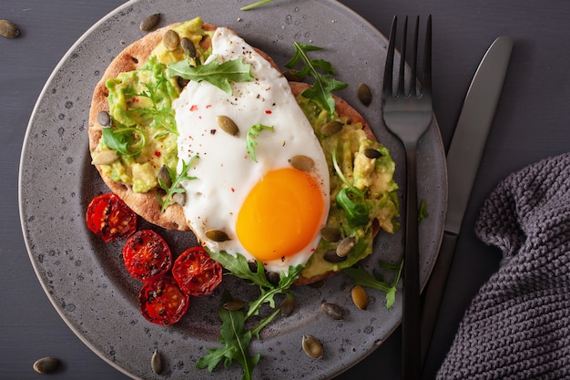 Panino dell'avocado della prima colazione con l'uovo fritto e il pomodoro