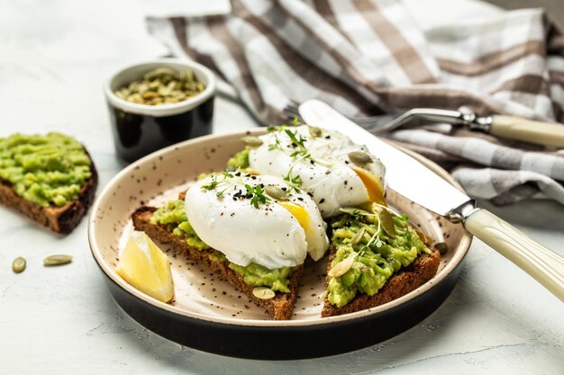 Panino di avocado con uovo in camicia e avocado su pane tostato Deliziosa colazione o spuntino su uno sfondo chiaro vista dall'alto