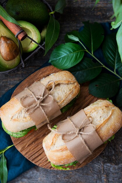 Panino di verdure fatto in casa con crema di formaggio, avocado fresco e pomodori su un tavolo di legno. Foto verticale. Vista dall'alto