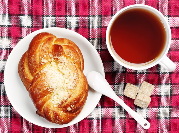 Panino dolce e tazza di tè su una tovaglia rossa. Vista dall'alto