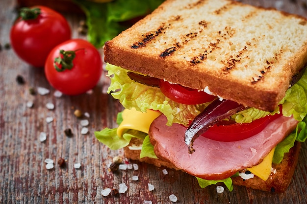 Panino fatto in casa con prosciutto, lattuga, formaggio e pomodoro su un fondo di legno