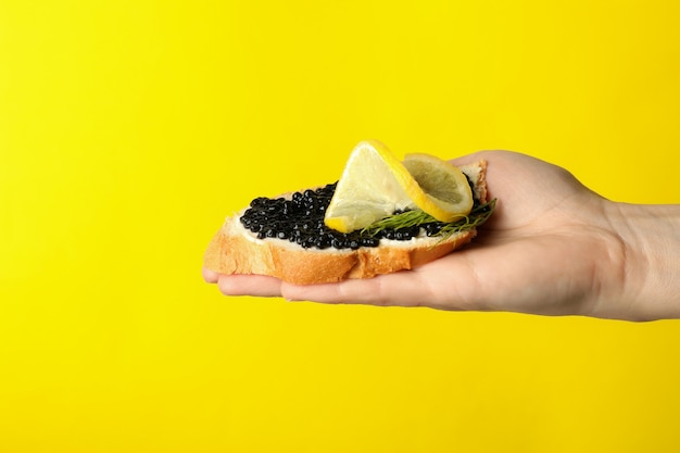 Panino femminile della stretta della mano con il caviale nero su colore giallo