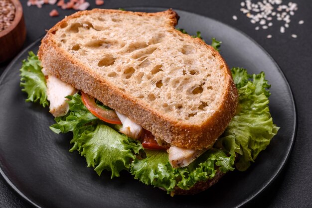 Panino fresco e gustoso con pomodori di pollo e lattuga su un piatto nero