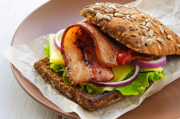 Panino hamburger con lattuga, pancetta, formaggio, cipolla e ketchup su carta