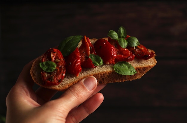 Panino in mano con pomodori secchi e basilico su sfondo scuro