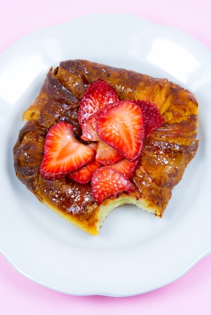 Panino o rotolo di pasta sfoglia morso. Torta con fragole fresche. Deliziosa tentazione di dolci e dessert su sfondo rosa.