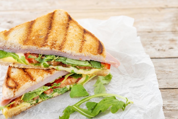 Panino panini con prosciutto, formaggio, pomodoro e rucola su tavolo di legno