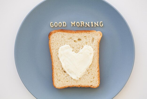 Panino per colazione a forma di cuore con formaggio su un piatto blu iscrizione buongiorno