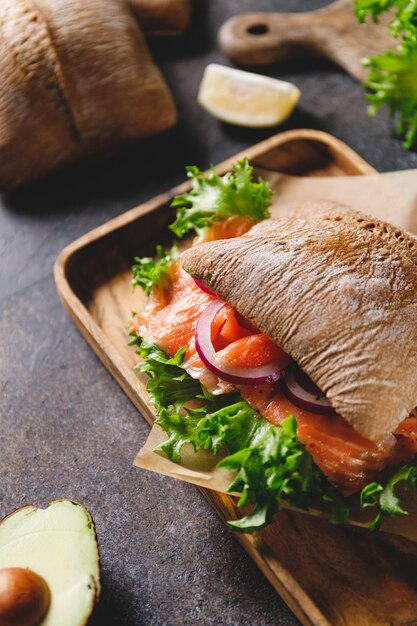 Panino sano con panino di pane di segale salmone avocado cipolla e insalata servito su una tavola rustica di legno