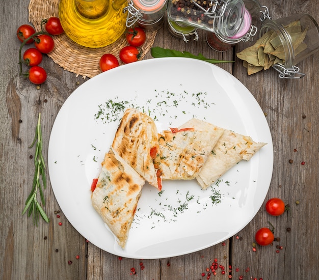 Panino Shawarma con verdure fresche e salsa sul piatto grigio decotated con pomodorini, foglie di basilico sul tavolo grigio
