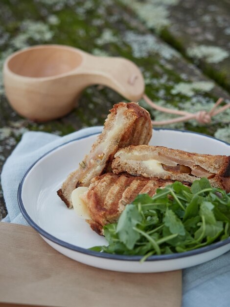 Panino tagliato a metà su un piatto con insalata di rucola su un tavolo da picnic in legno all'aperto